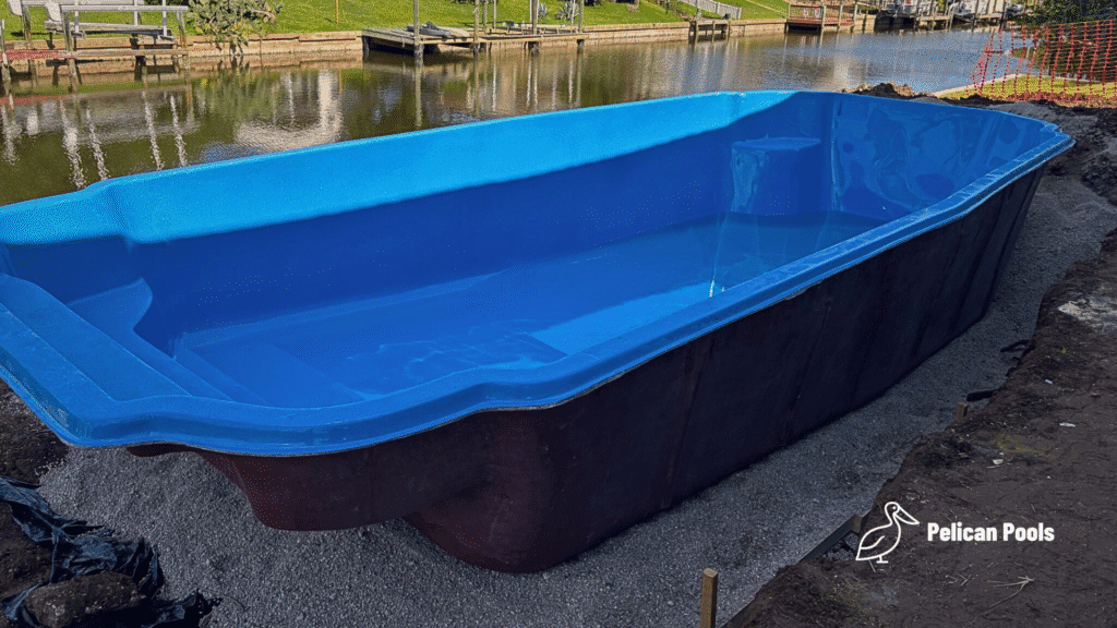 Fiberglass pool shell set in place beside a canal, partial fill with water.