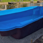 Fiberglass pool shell set in place beside a canal, partial fill with water.