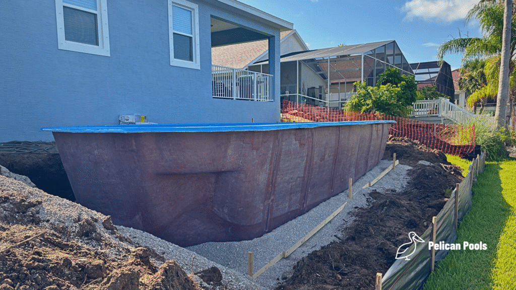 Fiberglass pool shell beside home foundation during installation.