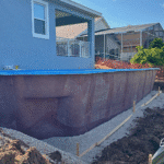 Fiberglass pool shell beside home foundation during installation.