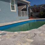 Fiberglass pool filled and surrounded by travertine deck next to home.