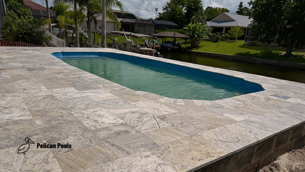 Fiberglass pool with travertine paver deck overlooking canal.