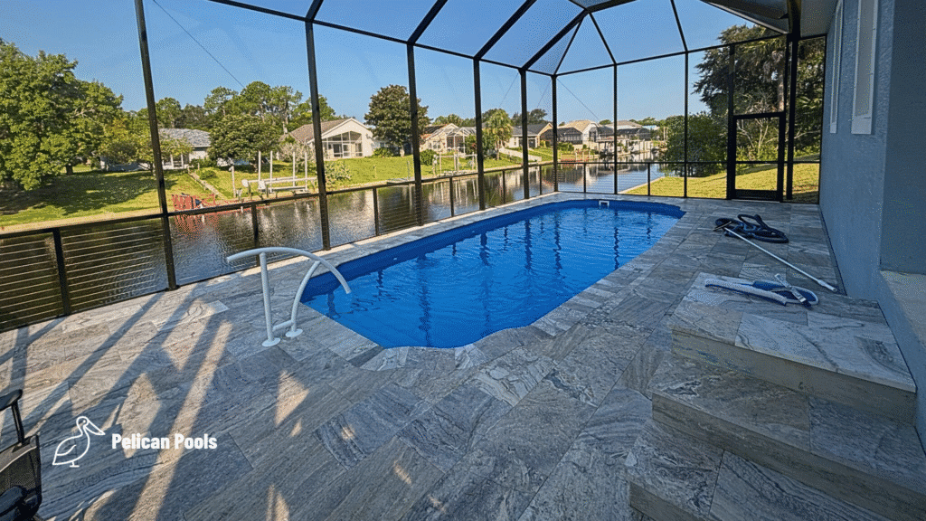 Enclosed fiberglass pool with travertine deck under screened lanai.