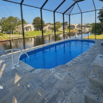 Enclosed fiberglass pool with travertine deck under screened lanai.
