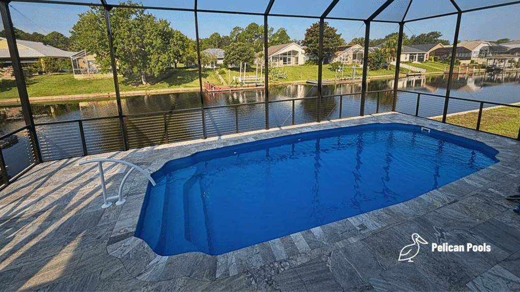 Blue fiberglass pool with travertine deck enclosed by screen overlooking canal.
