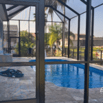 Screened enclosure surrounding a fiberglass pool viewed from the lanai door.