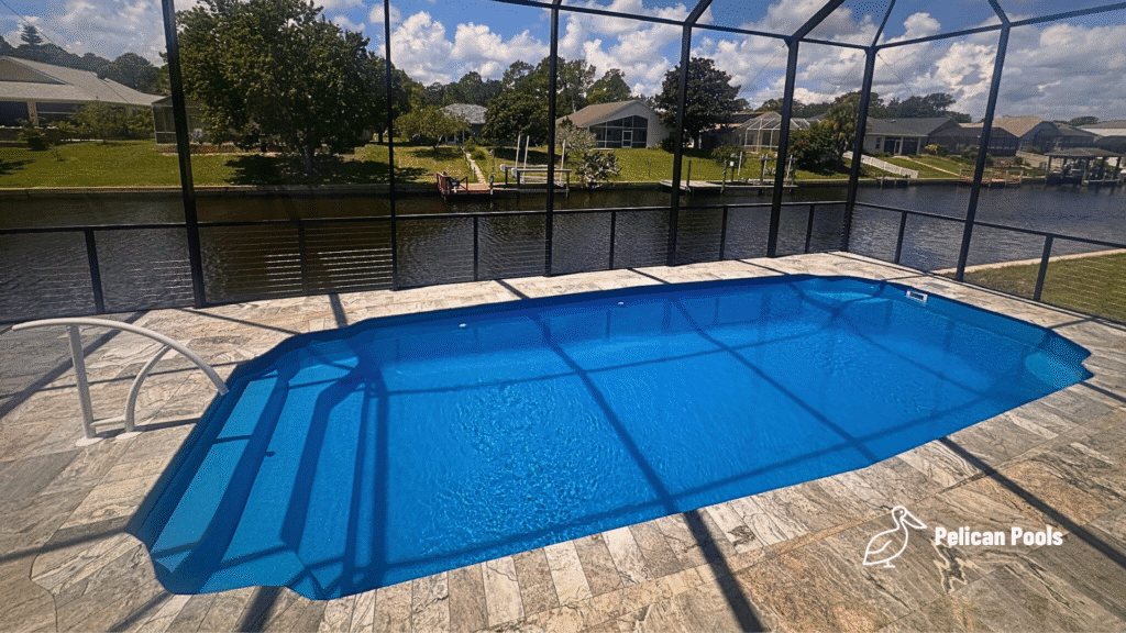Fiberglass pool with white railing steps and travertine deck beside canal.