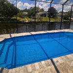 Fiberglass pool with white railing steps and travertine deck beside canal.