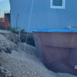 Fiberglass pool shell positioned close to house wall, surrounded by gravel.