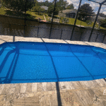 Elevated view of fiberglass pool showing deck pattern and canal reflection.