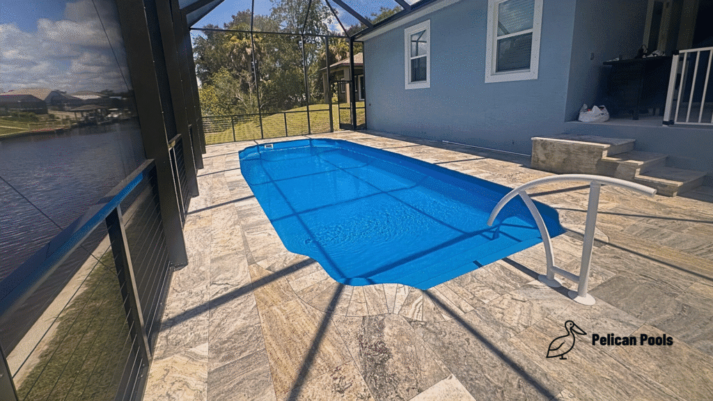 Blue fiberglass pool under screened lanai showing smooth travertine stairs.