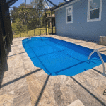 Blue fiberglass pool under screened lanai showing smooth travertine stairs.