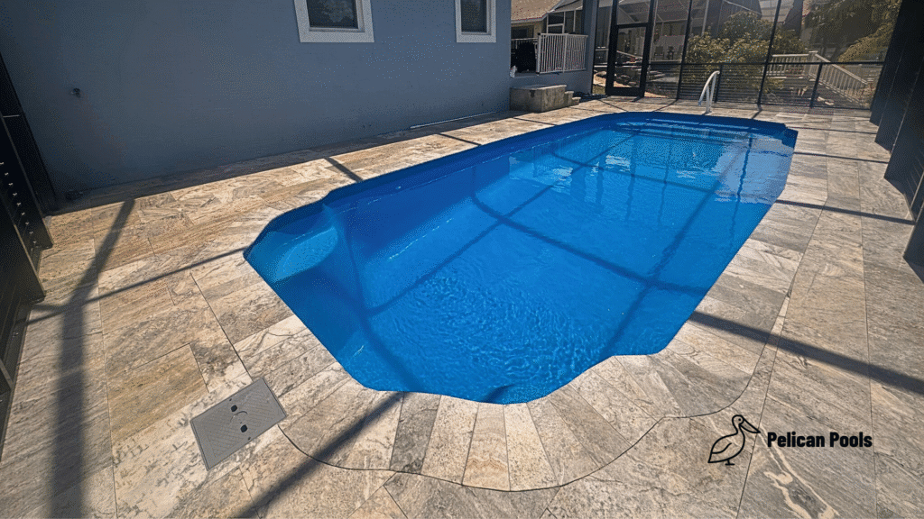 Hawaiian fiberglass pool with blue water and travertine deck beside home.