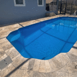 Hawaiian fiberglass pool with blue water and travertine deck beside home.