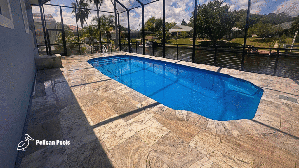 Side view of completed fiberglass pool under screened enclosure with canal backdrop.