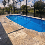 Side view of completed fiberglass pool under screened enclosure with canal backdrop.