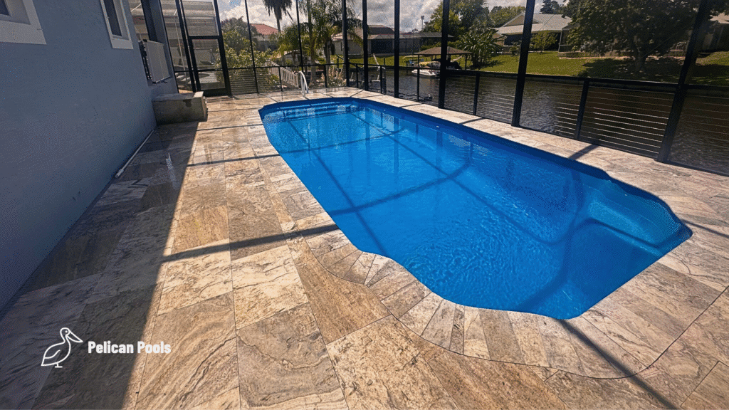 Travertine pool deck and fiberglass shell reflecting sunlight through screened lanai.
