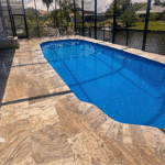 Travertine pool deck and fiberglass shell reflecting sunlight through screened lanai.