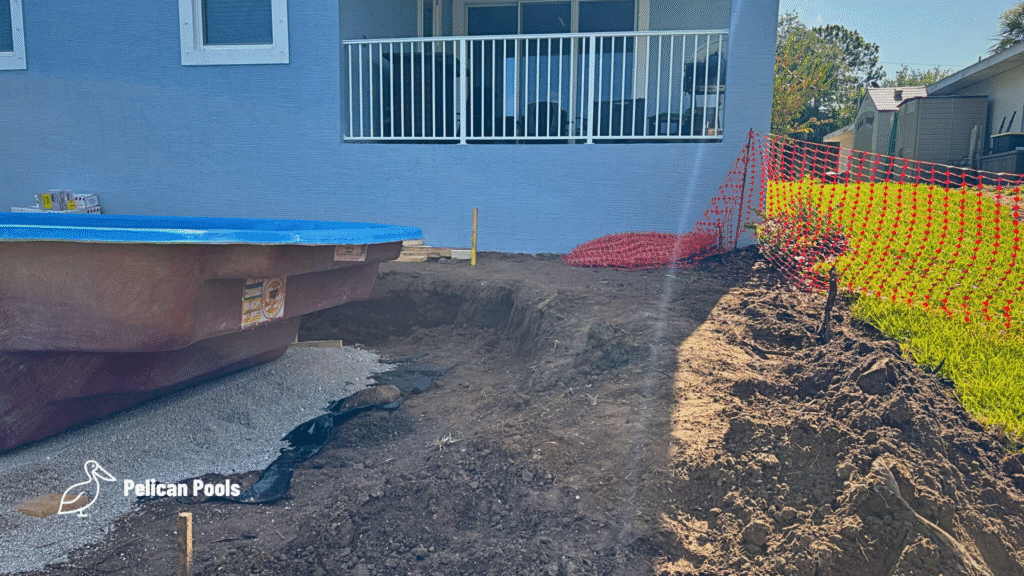 Rear view of fiberglass pool excavation area next to house patio.