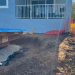 Rear view of fiberglass pool excavation area next to house patio.
