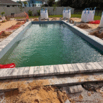 Newly installed fiberglass pool filled with water, surrounded by unfinished paver deck in Flagler Beach, FL.