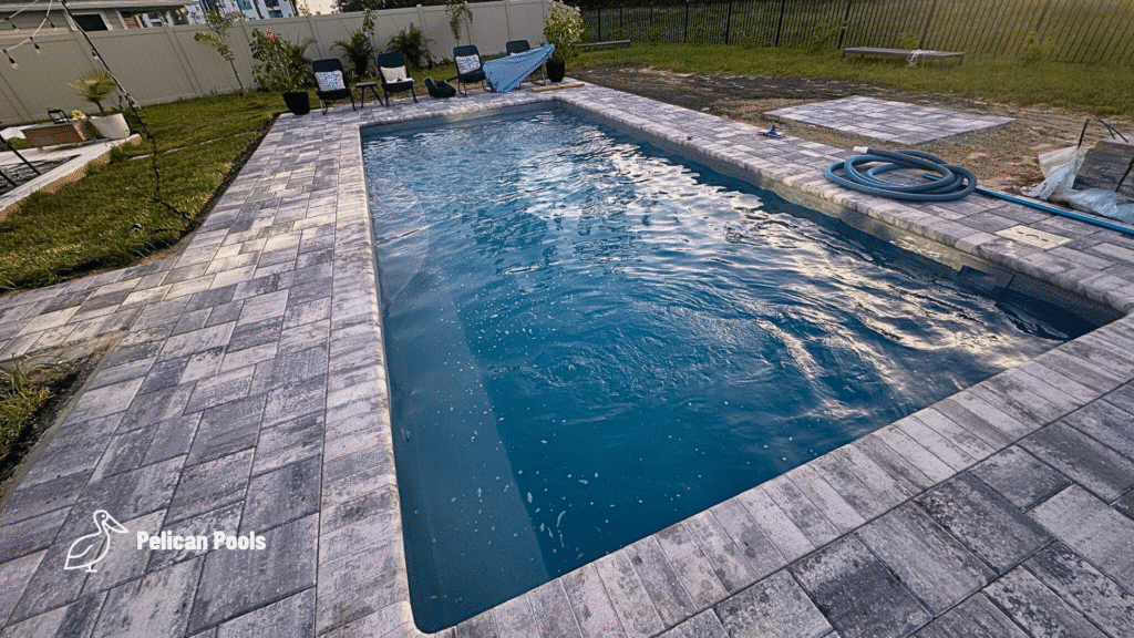 Rectangular blue-water fiberglass pool with gray paver coping and poolside lounge chairs.