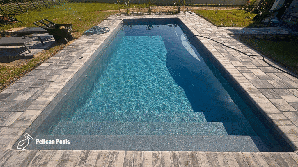 Rectangular blue-water fiberglass pool with gray paver coping and poolside lounge chairs.