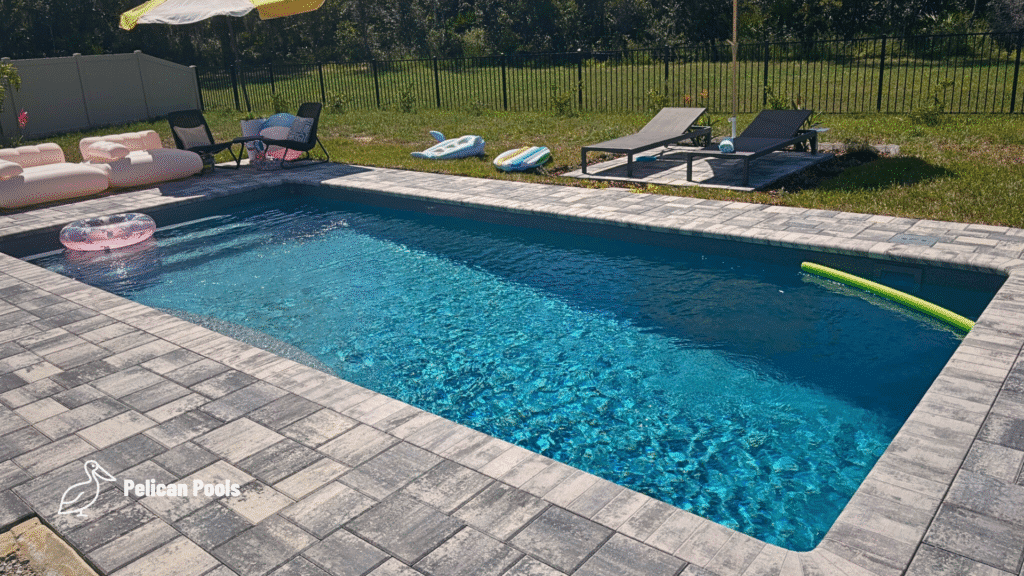 Finished pool deck with gray pavers, pool toys and umbrella-covered seating area.