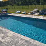 Finished pool deck with gray pavers, pool toys and umbrella-covered seating area.