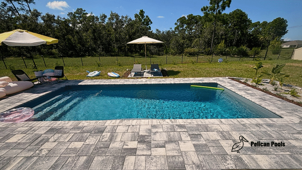 High-angle view of backyard pool and new paver deck with lush lawn beyond.