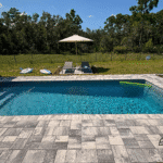High-angle view of backyard pool and new paver deck with lush lawn beyond.