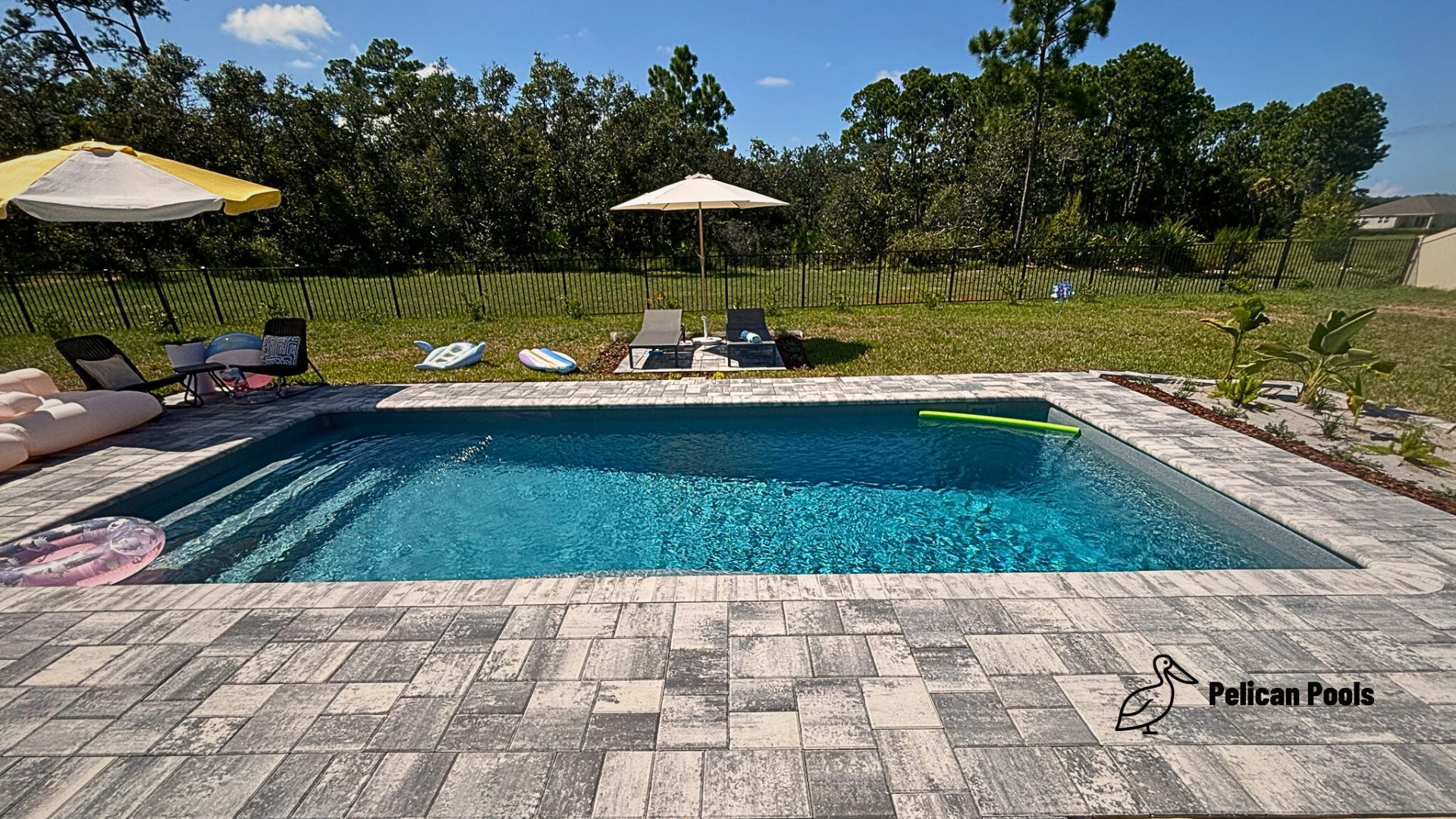 High-angle view of backyard pool and new paver deck with lush lawn beyond.