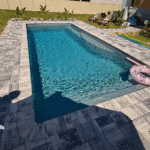 View of pool from corner deck edge showing steps into water and paver surround.