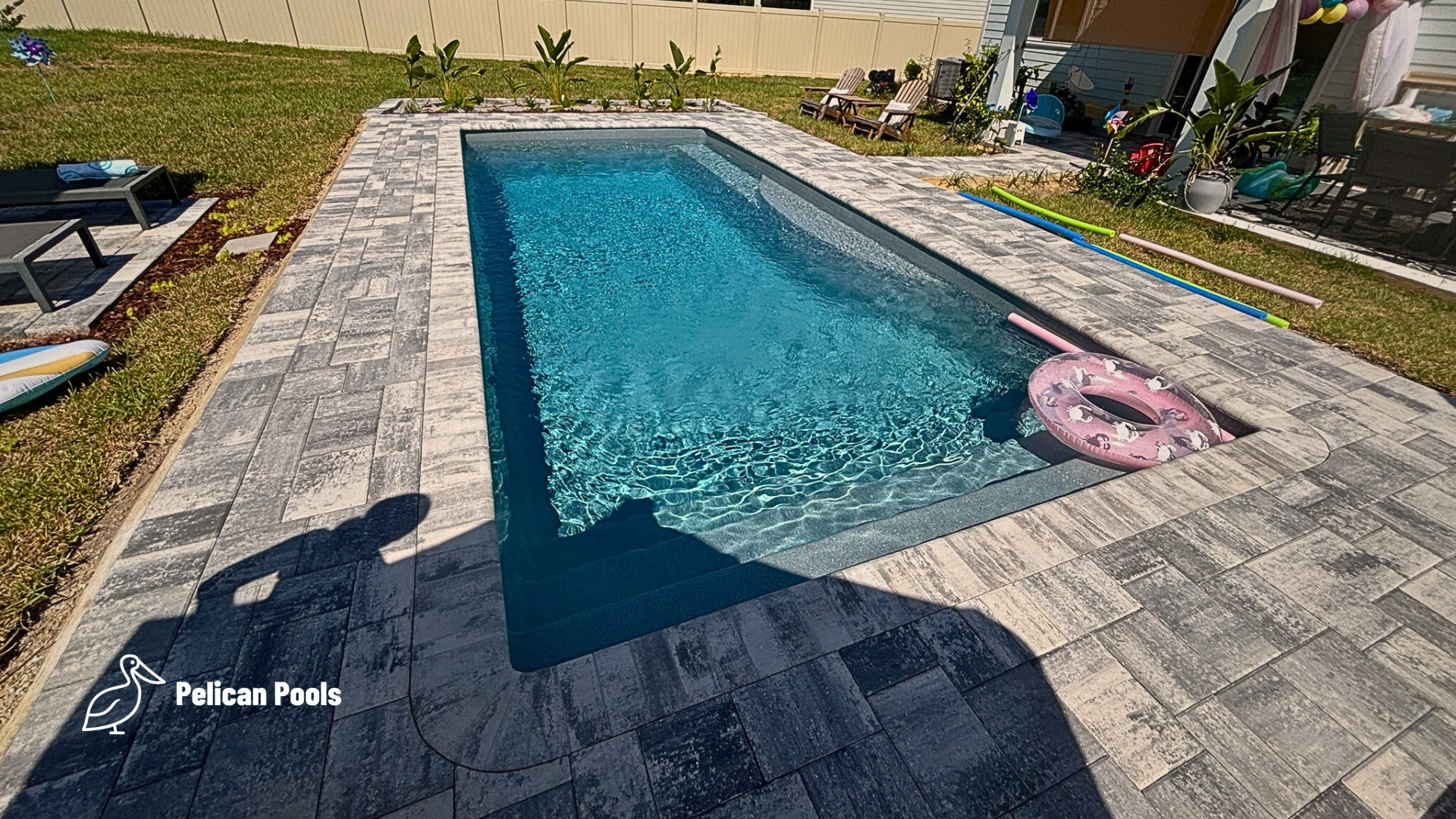 View of pool from corner deck edge showing steps into water and paver surround.