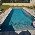 Pool with paver deck, surfboard-style float, and poolside garden beds.