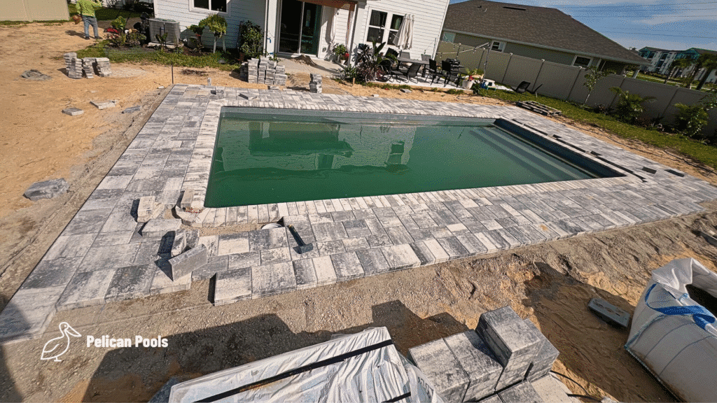 Rectangular fiberglass pool with gray paver coping in progress.