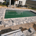 Rectangular fiberglass pool with gray paver coping in progress.