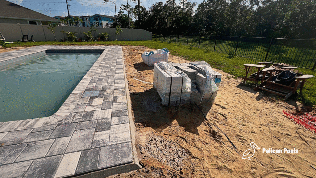Pool deck construction with gray pavers and sand fill.