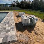 Pool deck construction with gray pavers and sand fill.