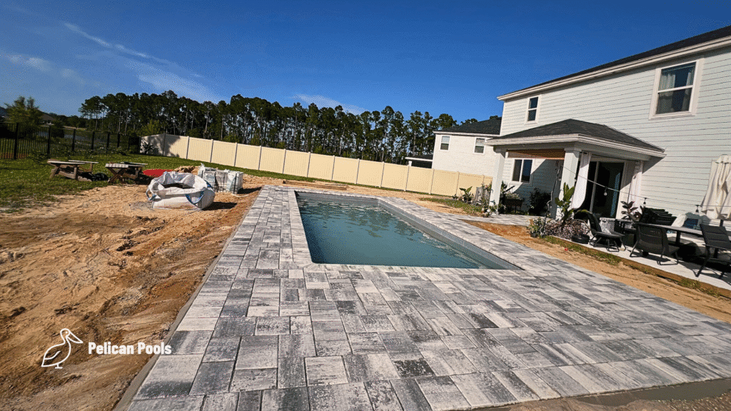 Backyard fiberglass pool with gray paver deck and open yard view.