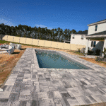 Backyard fiberglass pool with gray paver deck and open yard view.