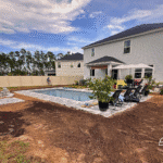 Completed fiberglass pool installation with patio furniture and garden plants.