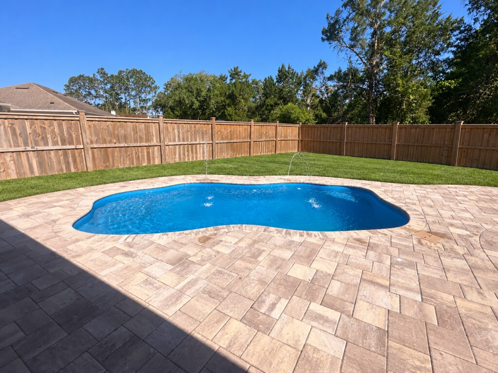 Ariella pool installation with existing stone pavers and water jets; backyard clutter removed and lawn digitally enhanced.