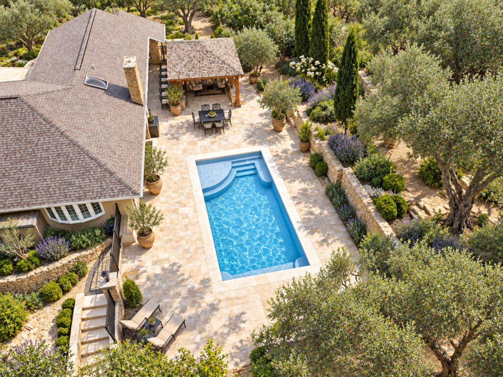 Aerial view of a San Juan Lake Superior pool showing its curved shallow shelf, entry steps and opposite bench beside an olive garden and limestone terrace.