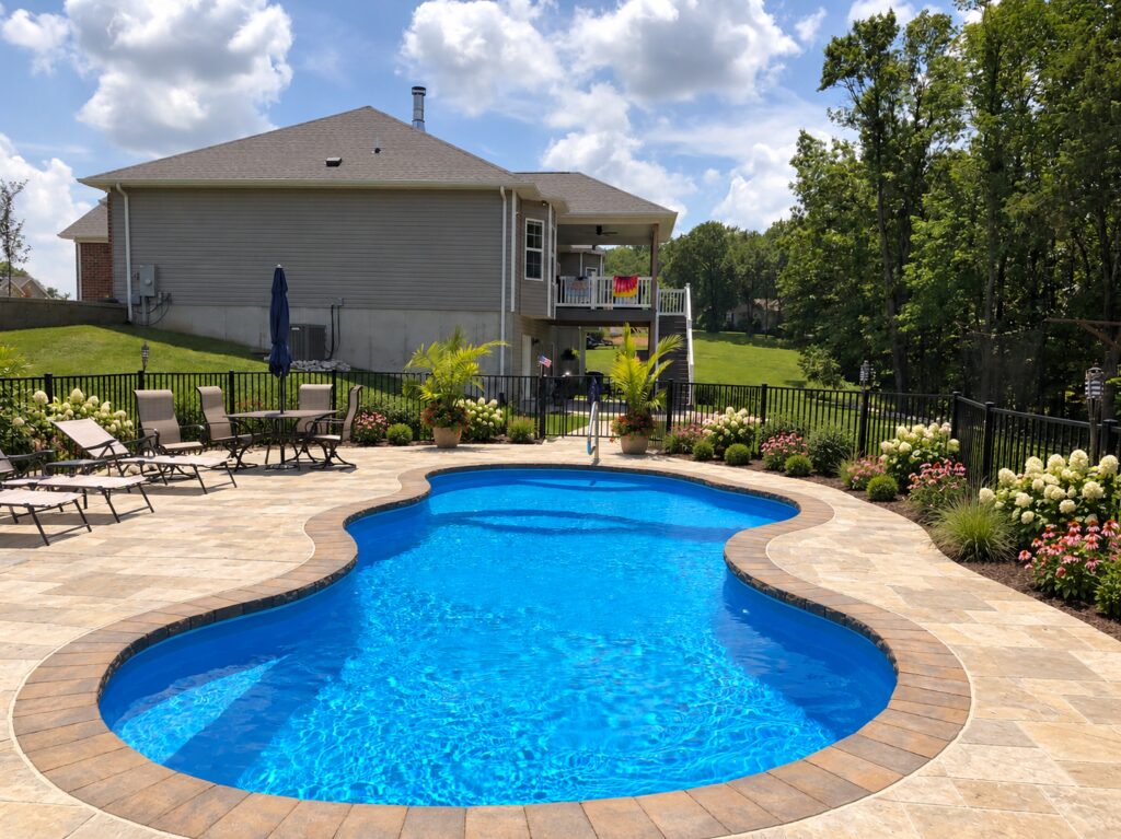 Edited design inspiration showing a Costa Azul pool with stone patio, flowering garden beds and black safety fence beside a home.