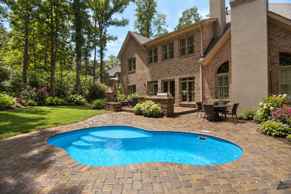 Edited design inspiration showing a Crystal Cove pool with curved steps and brick paver patio beside a wooded residential garden.