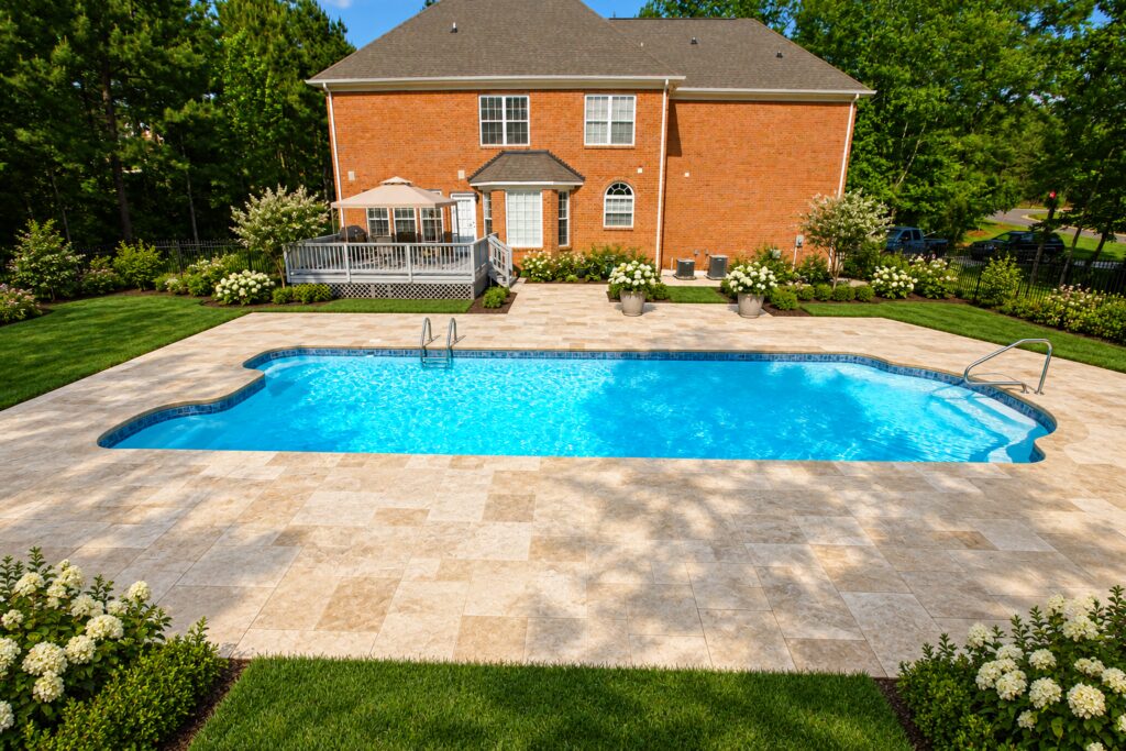 Dallas pool with travertine patio and flowering borders beside a brick house. Digitally edited design inspiration.